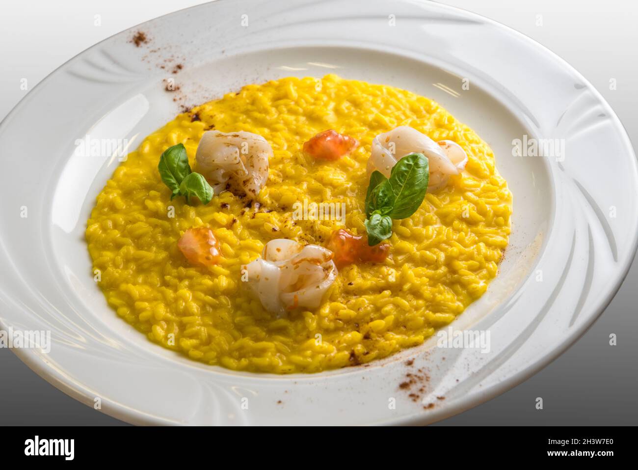 Gelbes Safranrisotto mit Tintenfisch, Basilikumblättern und frischem Tomatenmark, Gourmet-Rezept in einem weißen Gericht Stockfoto