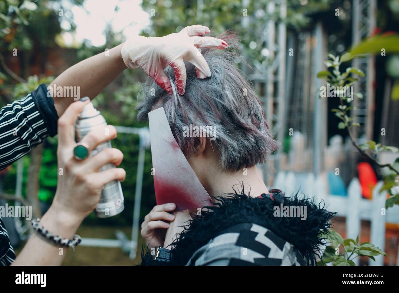 Friseur Stylisten Make-up Artist färbt das Haar eines jungen Mannes mit einem geschlossenen Gesicht aus einer Aerosoldose Stockfoto