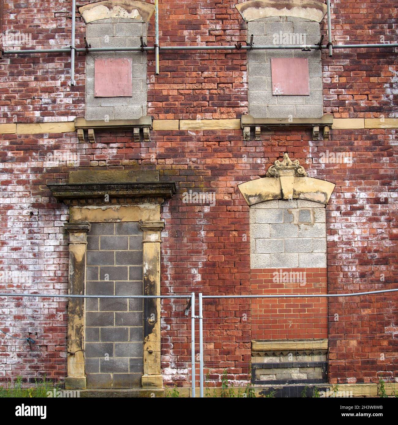 Fassade eines verlassenen, verlassenen alten Hauses mit zerbröckelnden Ziegelwänden und versperrten Fenstern Stockfoto