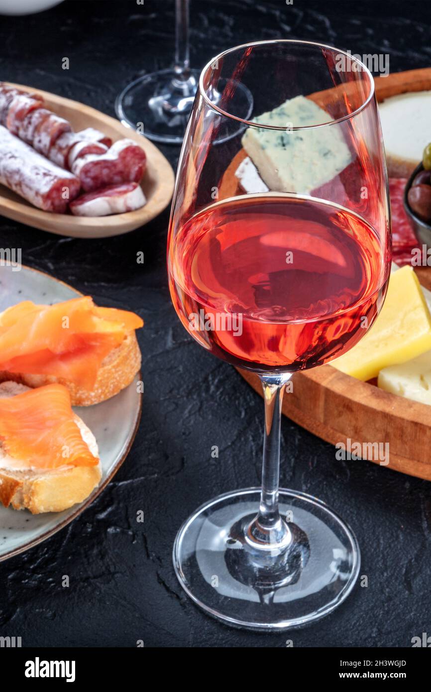 Ein Glas Roséwein mit Lachs-Sandwiches, Käse und Wurstwaren Stockfoto