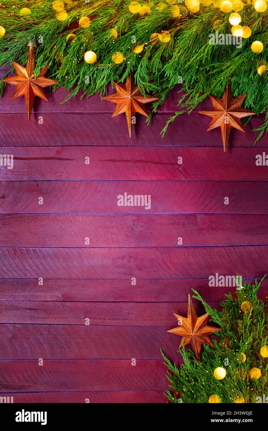 Textur aus roten und violetten Brettern mit Zweigen aus grünem Thuja und orangefarbenen Sternen mit gelbem Bokeh. Weihnachten, Neujahr. Vertikal. Speicherplatz kopieren Stockfoto