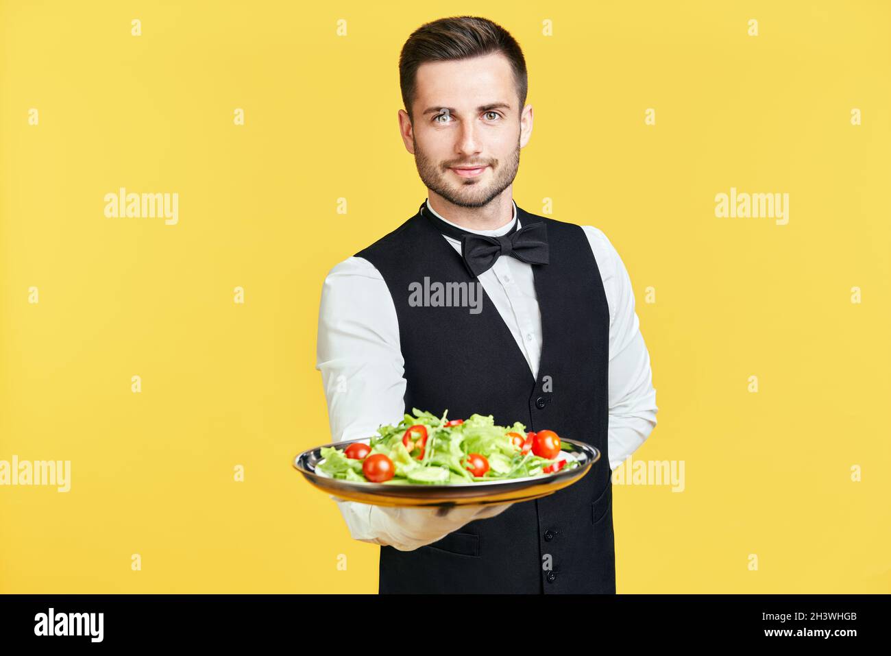 Ein fröhlicher Kellner hält einen Teller mit gesundem Gemüsesalat bereit Stockfoto