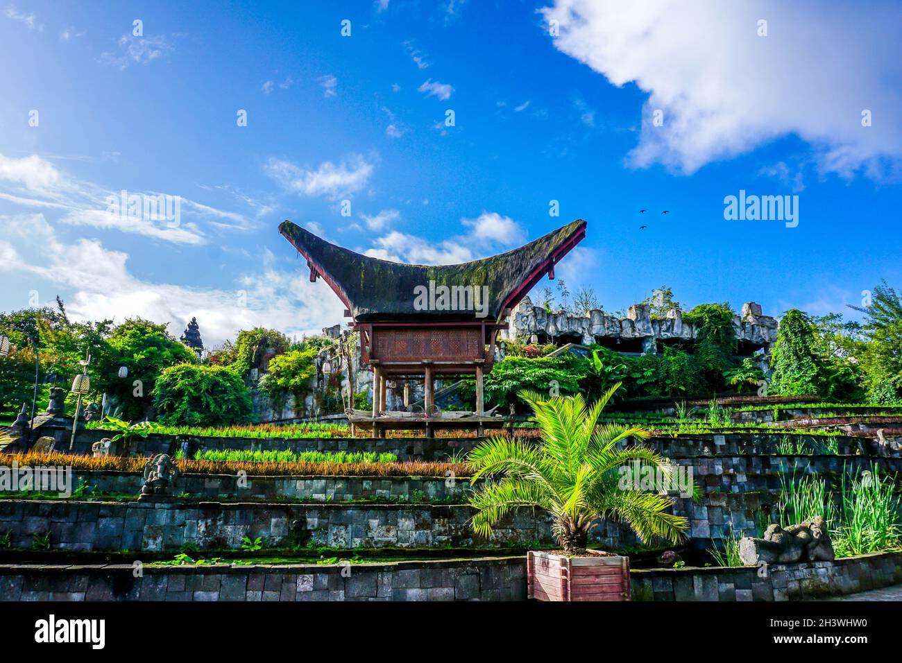 Atemberaubende Aussicht auf hängende Gärten mit zahlreichen Pflanzen, Blumen und Palmen, alte Gebäude, Statuen und Vögel im bewölkten Himmel Stockfoto