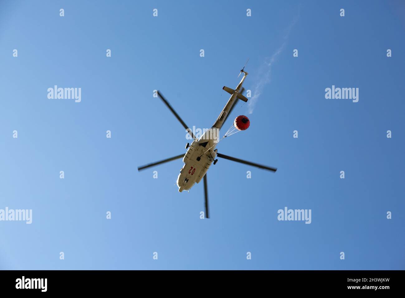 Hubschrauber fährt in den Feuerbereich, um Waldbrände zu löschen. Helikopter mit Wassereimer am blauen Himmel. Stockfoto