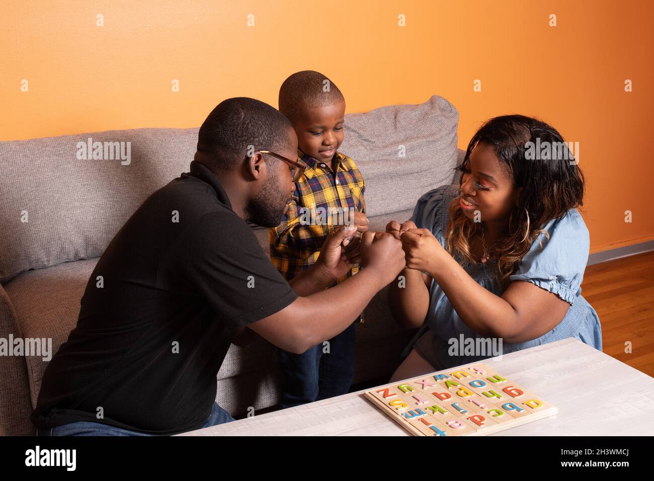 Vorschulkind zu Hause mit Eltern alle tun Faust Beule Glückwünsche, nachdem Junge beendet ABC Puzzle Stockfoto
