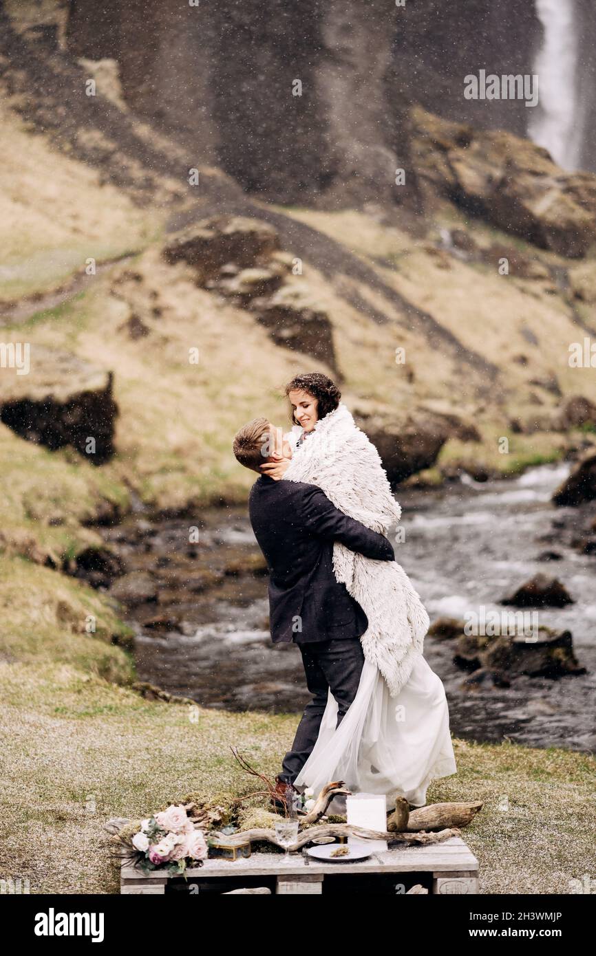 Reiseziel Island Hochzeit, in der Nähe des Kvernufoss Wasserfalls. Hochzeitspaar am Ufer eines Bergflusses. Der Bräutigam trägt das bri Stockfoto