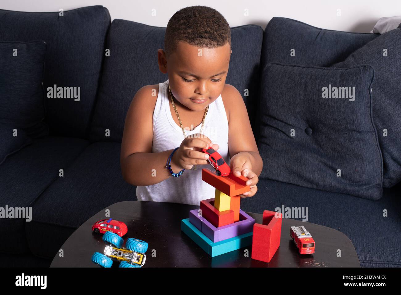 Kind im Vorschulalter zu Hause spielt mit Holzblöcken Puzzle und Spielzeugautos Stockfoto