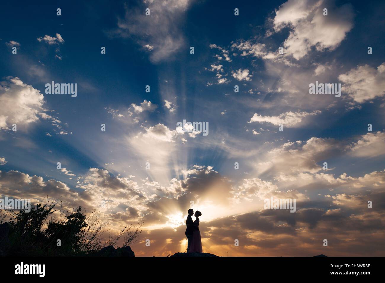 Die Braut und der Bräutigam umarmen sich zärtlich am Berg in den Strahlen der untergehenden Sonne Stockfoto