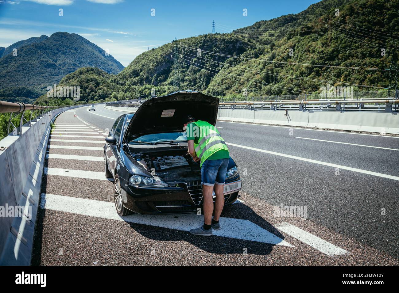 Mechaniker in reflektierender Weste versucht, ein defektes Auto auf der Autobahn, Motorhaube, zu reparieren Stockfoto