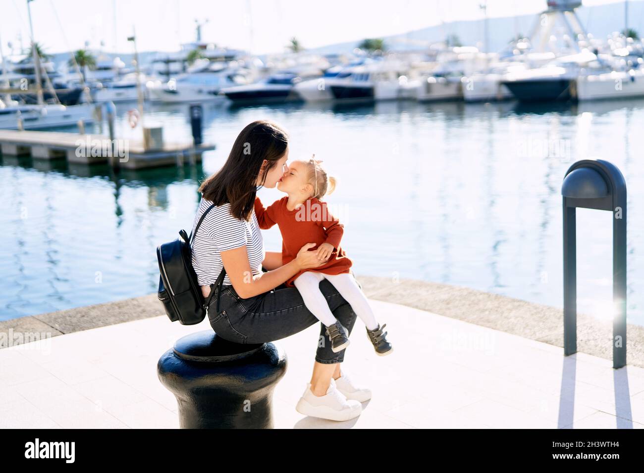 Mutter küsst ihr Baby Mädchen, während sie auf einem sitzt pier am Meer Stockfoto