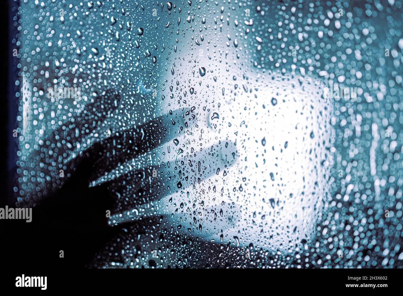 Depression und Auf Wiedersehen Konzept: Dunkle Silhouette der menschlichen Hand auf dem Fenster mit Regentropfen Stockfoto