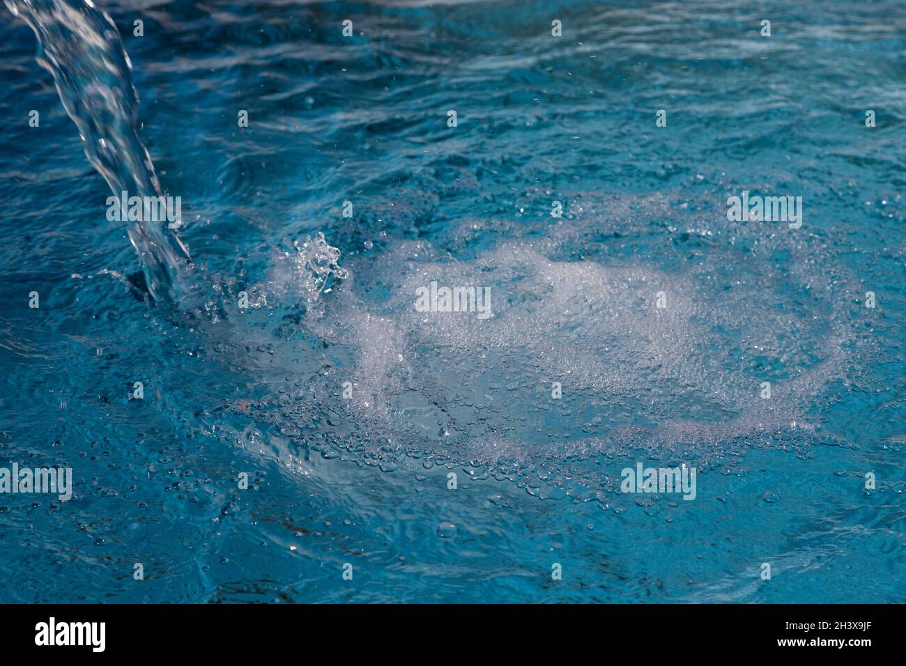 Sauberes Wasser, Blasen und Tropfen, die aus einer Quelle in den Pool fließen. Stockfoto