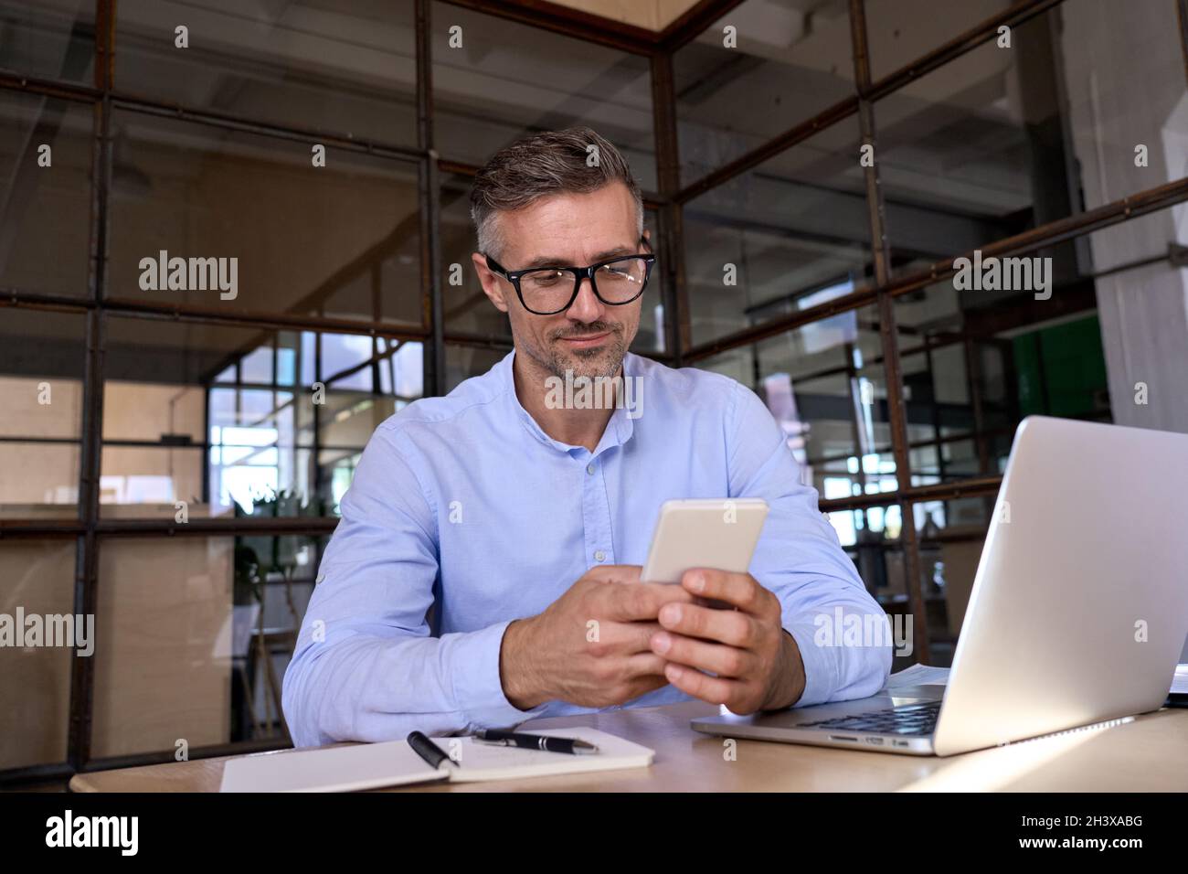 Kaukasischer Geschäftsmann hält sich in den Händen mit Smartphone im Büro mit Laptop. Stockfoto