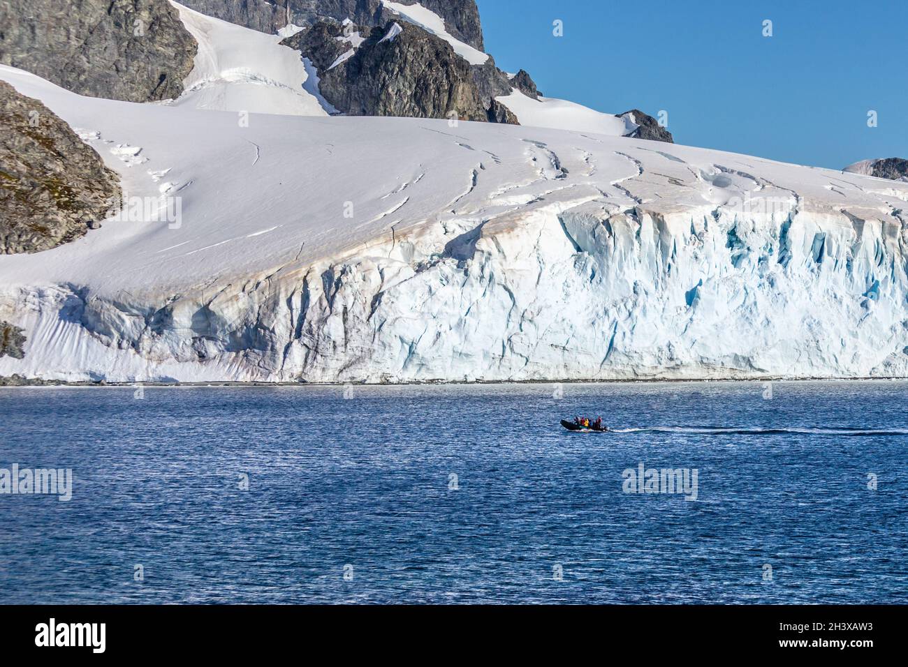 Boot voller Touristen, die an dem riesigen Gletscher in der Bucht nahe der Insel Cuverville, Antarktishalbinsel, vorbeifahren Stockfoto