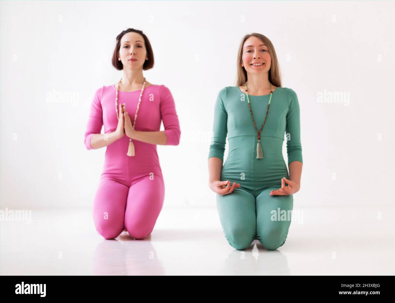 Zwei junge Frauen in langen Sport-Bodys, die gemeinsam Yoga-Asanas im Studio durchführen Stockfoto