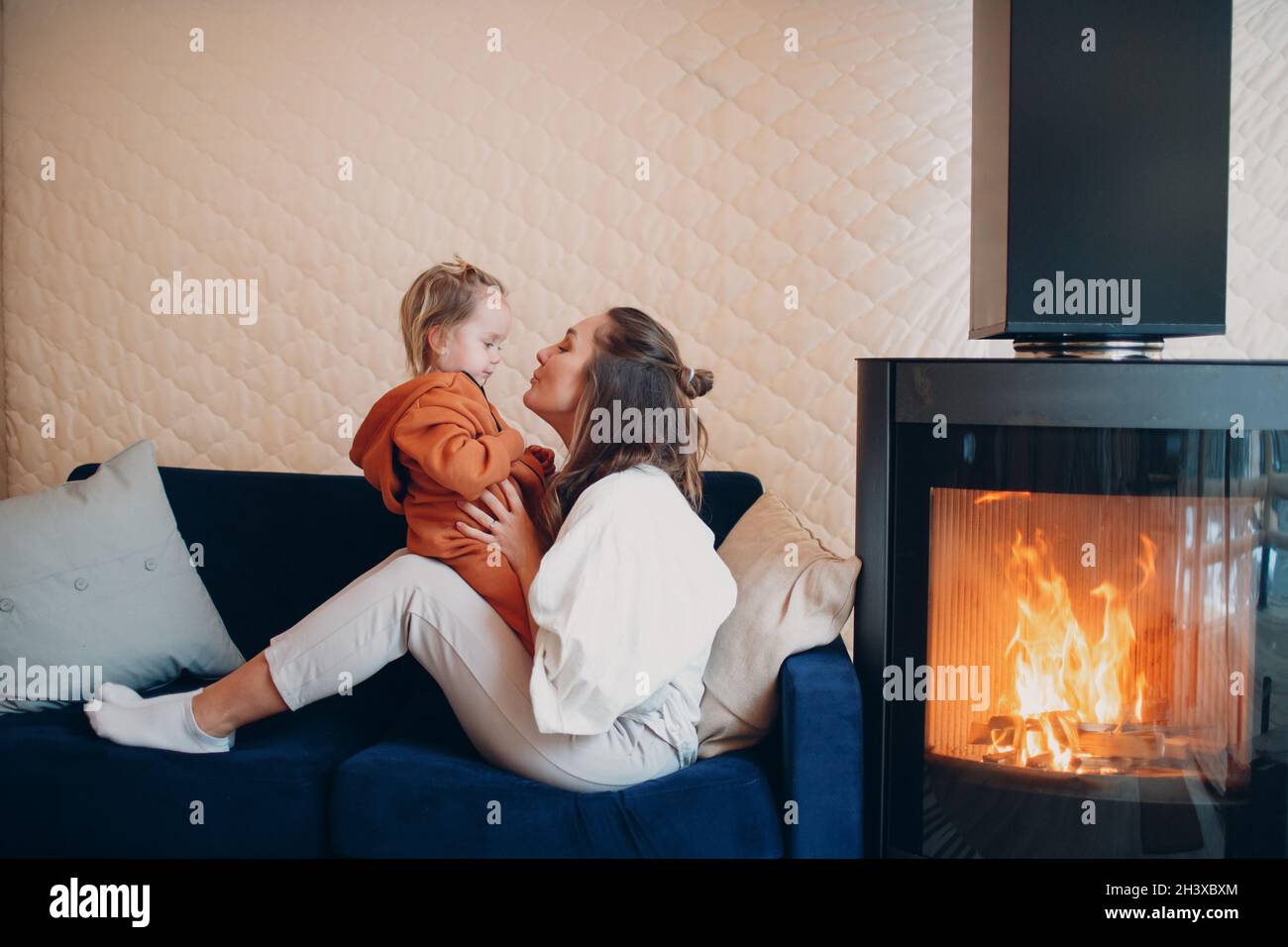 Mutter und Kind sitzen und spielen auf dem Sofa in der Nähe des Kamins. Mama und Baby. Eltern und kleine Kinder entspannen sich zu Hause. Familie hat Stockfoto