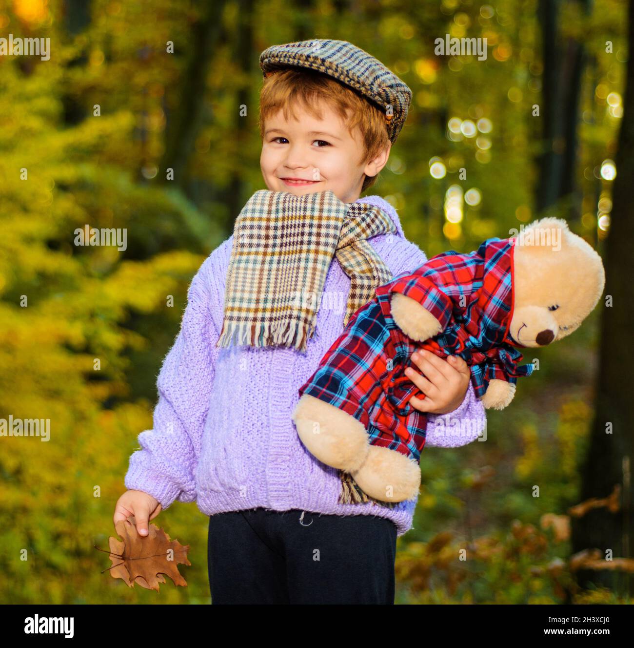 Herbstjunge. Schönes Kind in warmem Pullover. Kleiner Junge, der im Herbstpark mit Teddybären spielt. Stockfoto