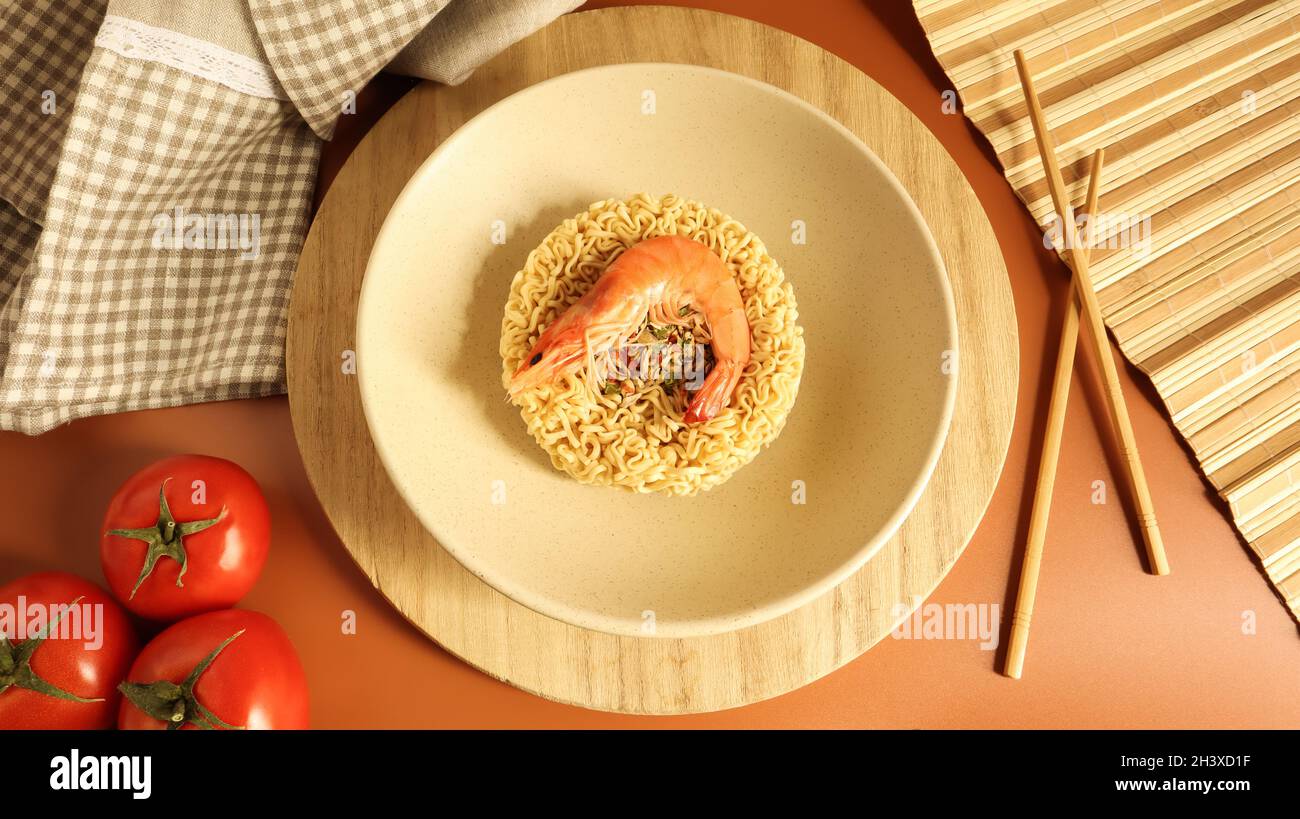 Scharfe Instant-Nudelsuppe mit Garnelen und Gemüse. Garnelensuppe, Kochen, Essen. Roh getrocknete kreisförmige vermicelli in einer Platte. Stockfoto