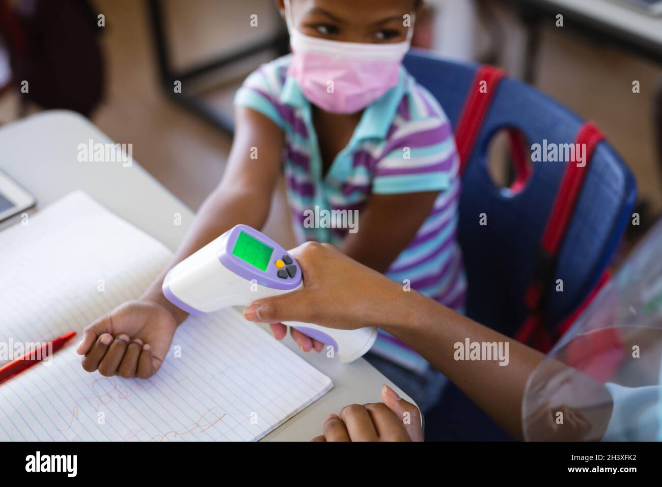 Mittlerer Abschnitt der weiblichen Gesundheitsarbeiterin, die die Temperatur eines Mädchens in der Grundschule misst Stockfoto