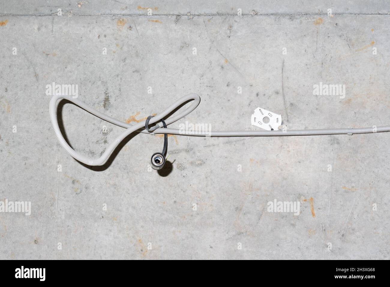 Dicker gedrehter grauer staubiger Draht, der mit einem Kabel aus der Wand ragt. Elektrokabel auf schmutziger weißgrauer beige roher rauer Wand Stockfoto