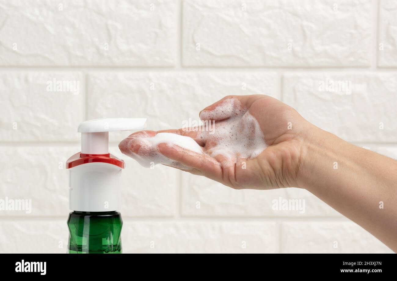 Weibliche Hand hält weißen Schaum aus einem Kunststoff-Spender gepresst, antiseptisch Stockfoto