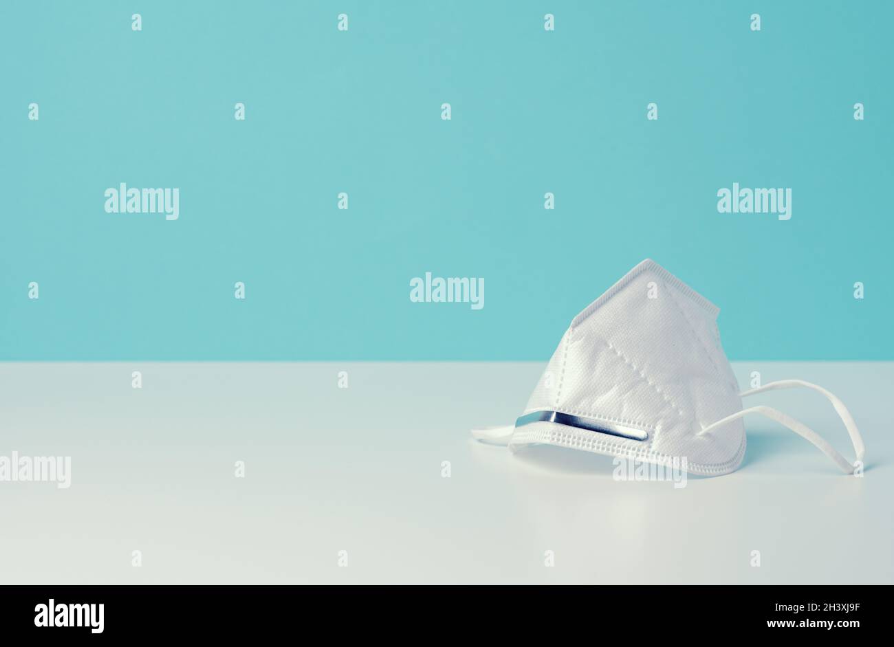 Weiße medizinische Einwegmaske auf blauem Hintergrund, persönliche Schutzausrüstung für die Atemwege vor Virusinfektion Stockfoto
