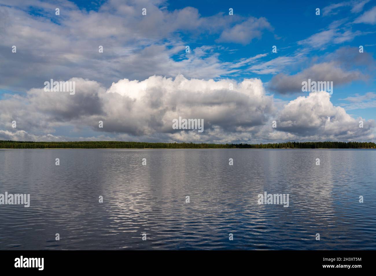 Eine ruhige und friedliche Seenlandschaft in der Wildnis mit Wald am fernen Ufer unter einem ausdrucksstarken blauen Himmel mit weißem c Stockfoto