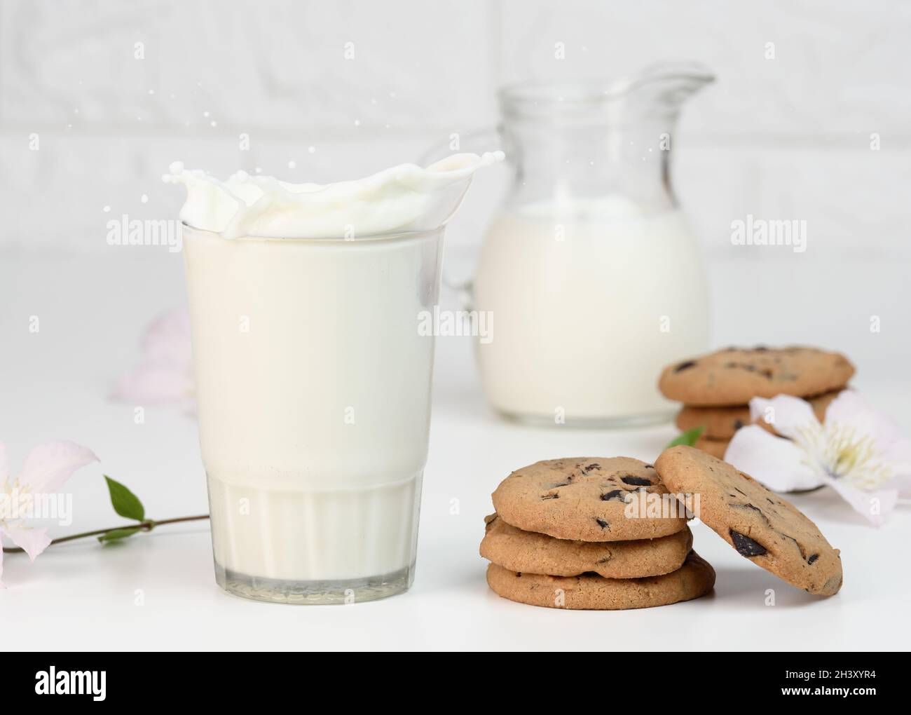 Volle Glas Tasse frische Milch mit Spritzern steht auf einem weißen Tisch, gesundes Frühstück Stockfoto