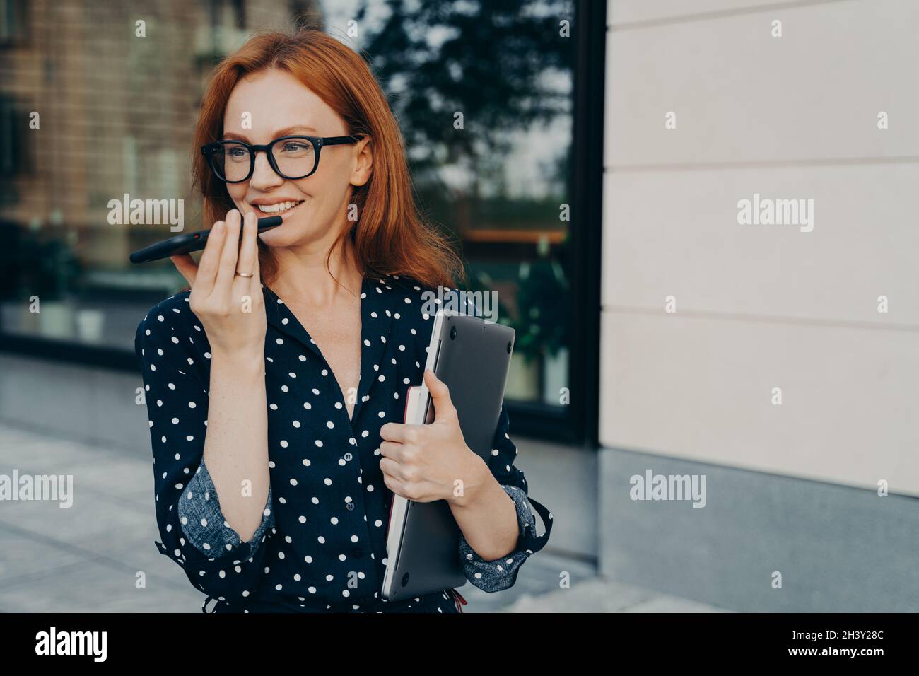 Schöne Geschäftsfrau steht mit dem Mobiltelefon im Freien und nimmt Audionachricht oder Smartphone auf Stockfoto
