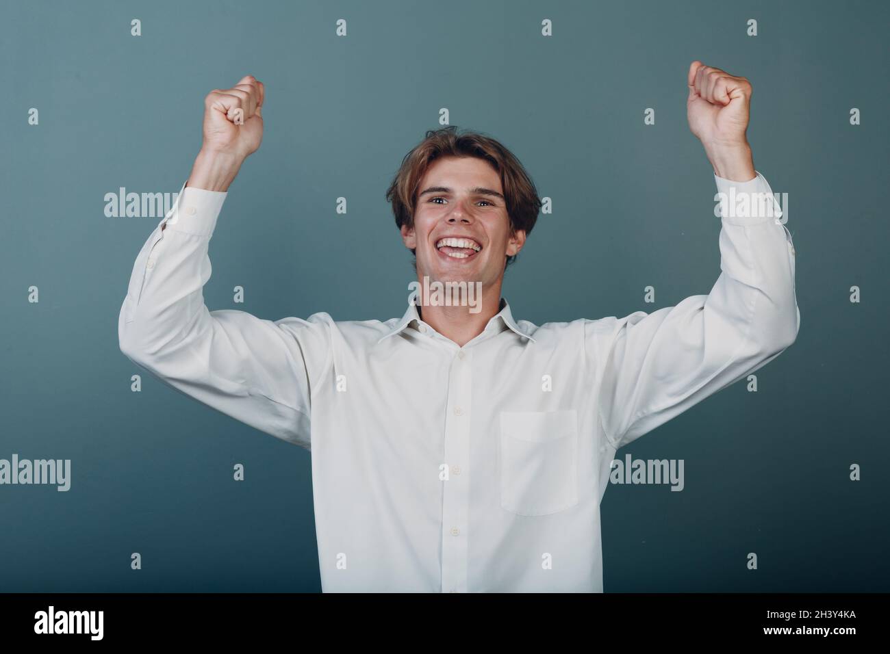 Der junge Mann gewinnt Freude und wirft seine Hände in die Höhe erhobene Arme in die Luft Stockfoto