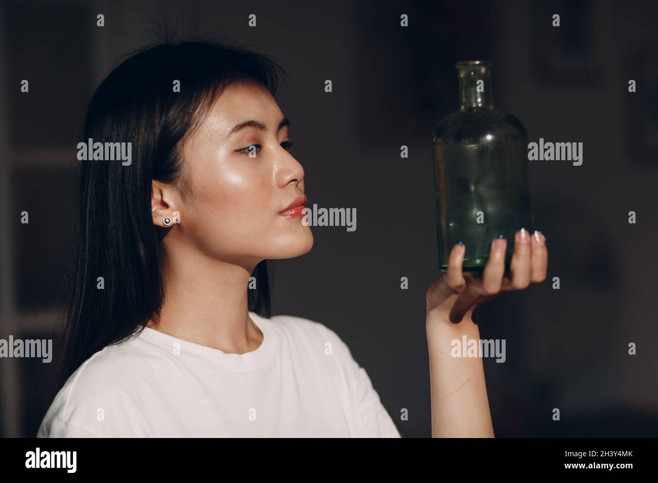 Asiatische junge Erwachsene Frau halten grüne Glasflasche Gesicht mit Tageslicht Stockfoto