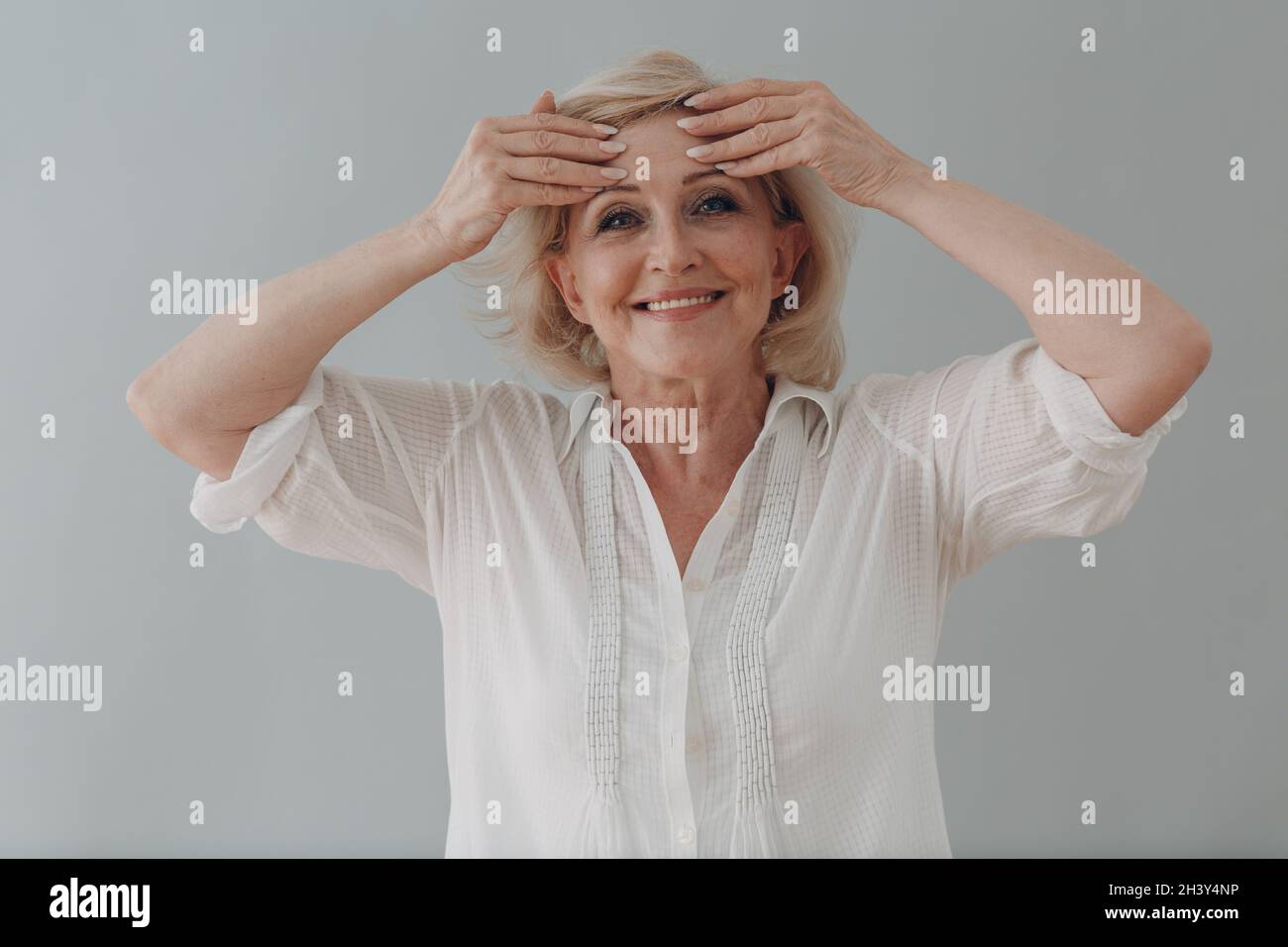 Ältere kaukasische alte Frau grauhaarige Porträt tun facebouding Yoga Gesicht Gymnastik Yoga Selbstmassage. Stockfoto