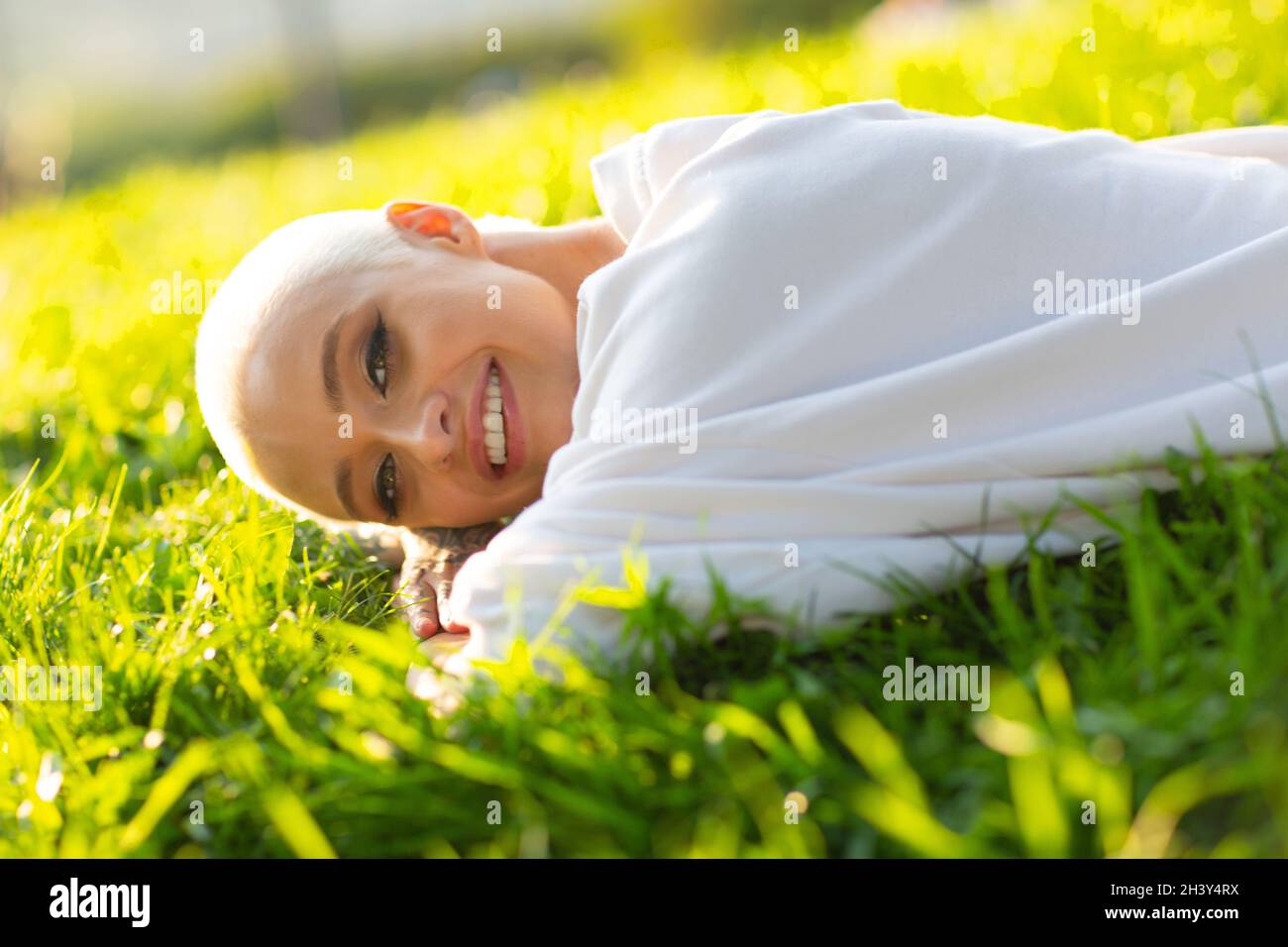 Millenial junge Frau blond kurze Haare im Freien lächelnd lag auf Gras Porträt. Stockfoto