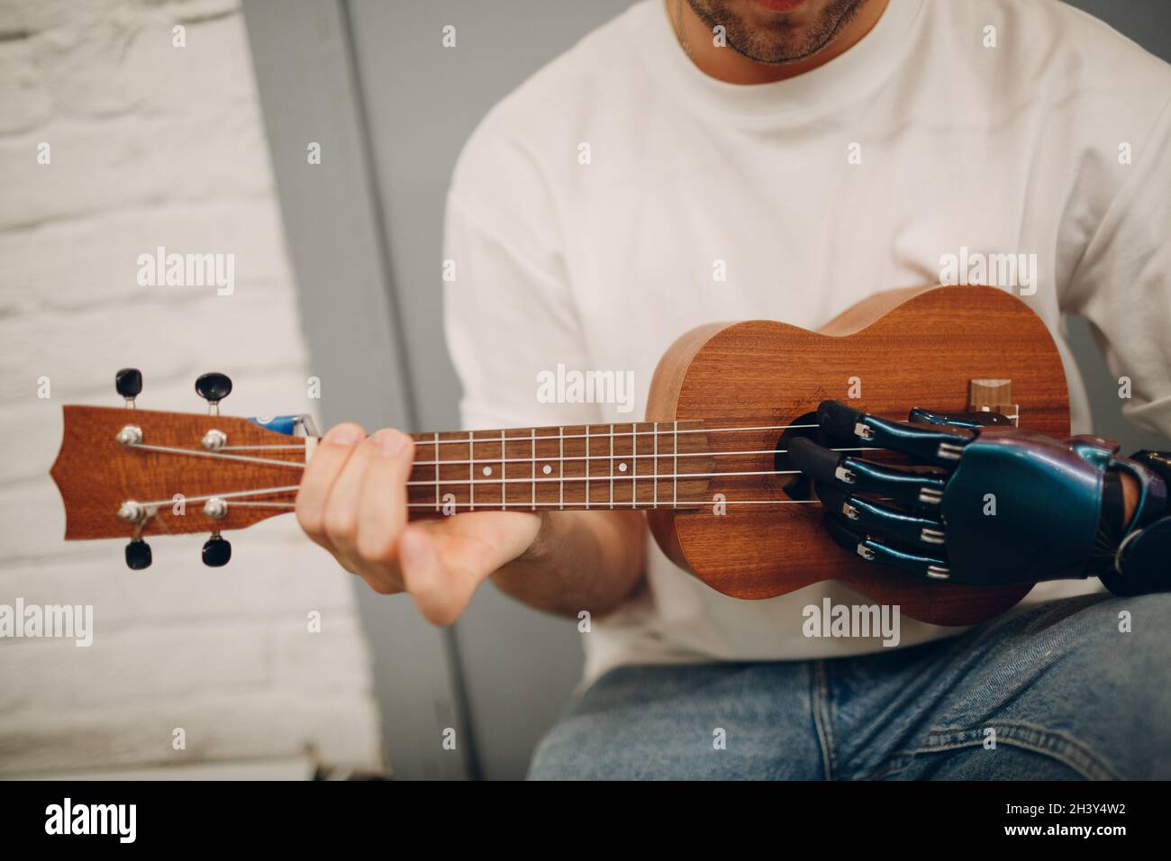 Junger behinderter Mann mit künstlicher prothetischer Hand spielt auf der Gitarre im Geschäft. Stockfoto