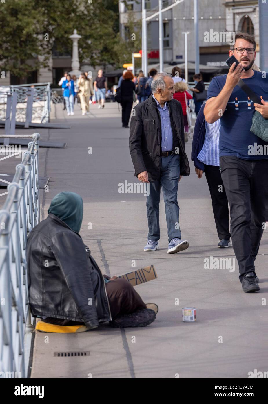 Fußgänger, die an einer Bettlerin auf der Pont de la Machine, Genf, Schweiz, vorbeikommen Stockfoto