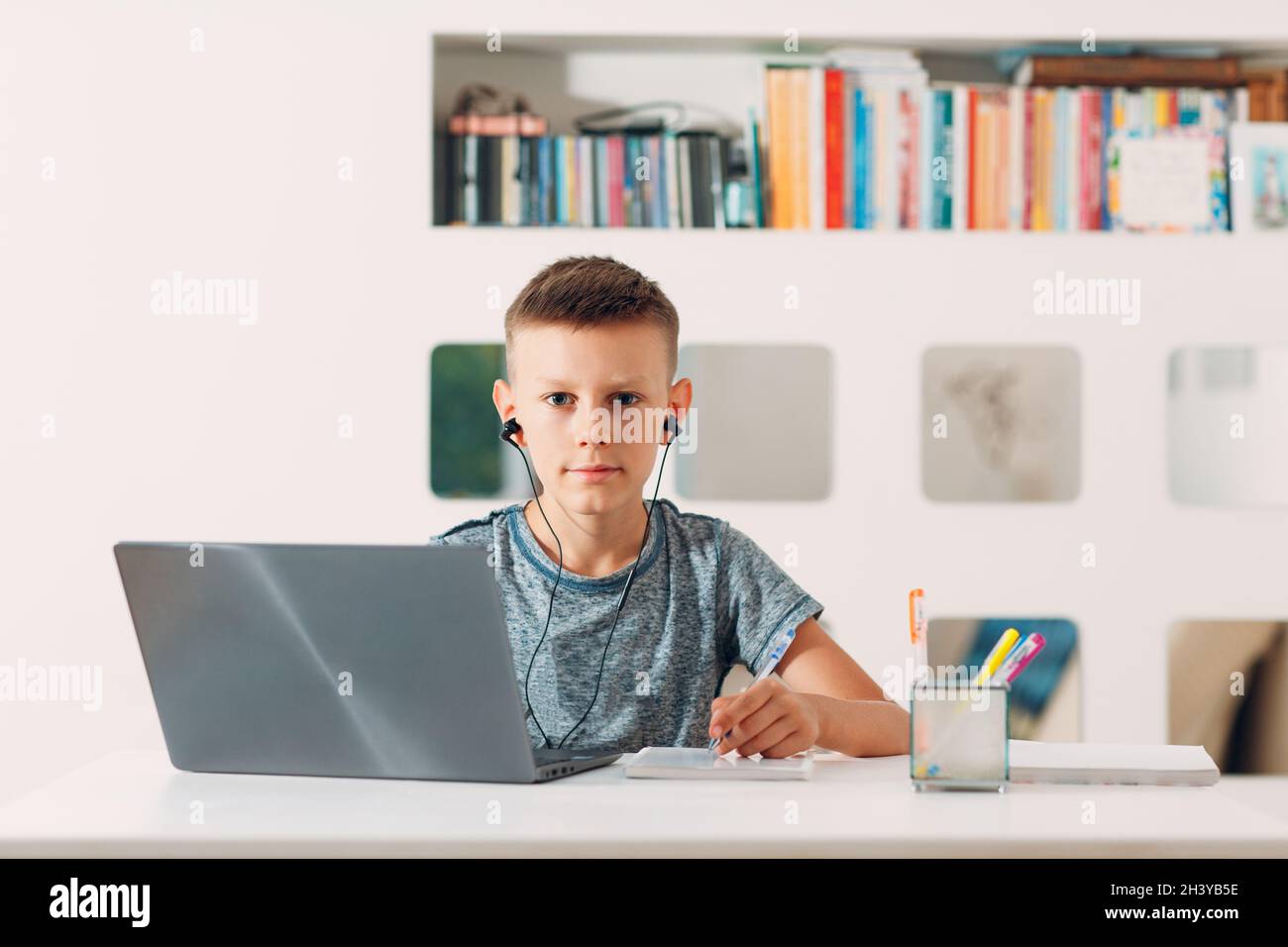 Kleiner Junge im Headset sitzt am Tisch mit Laptop und bereitet sich auf die Schule. Online-Bildungskonzept. Stockfoto