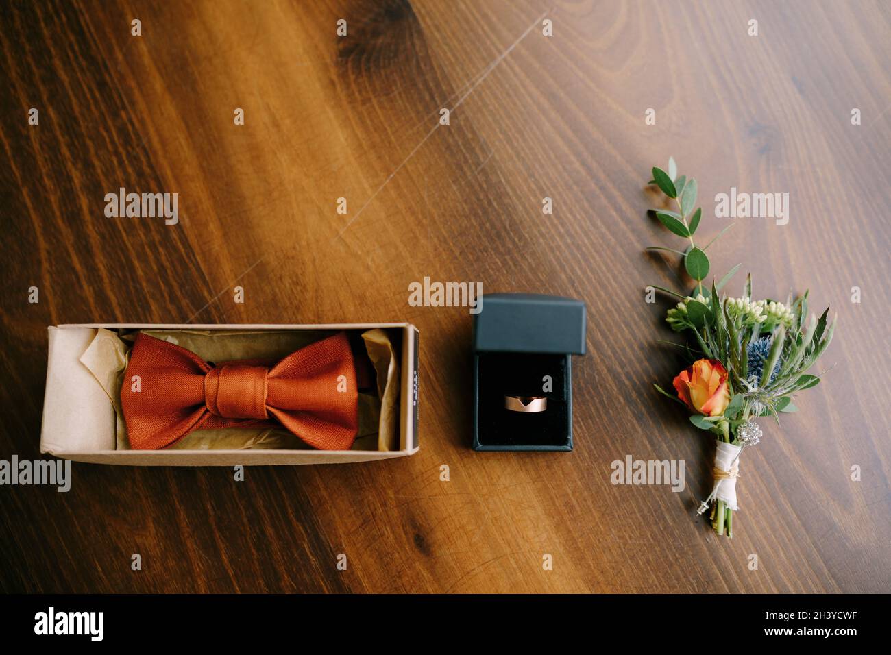 Accessoires für den Bräutigam Fliege, Gold Ehering und boutonniere auf einem Holzboden in einer Reihe. Stockfoto
