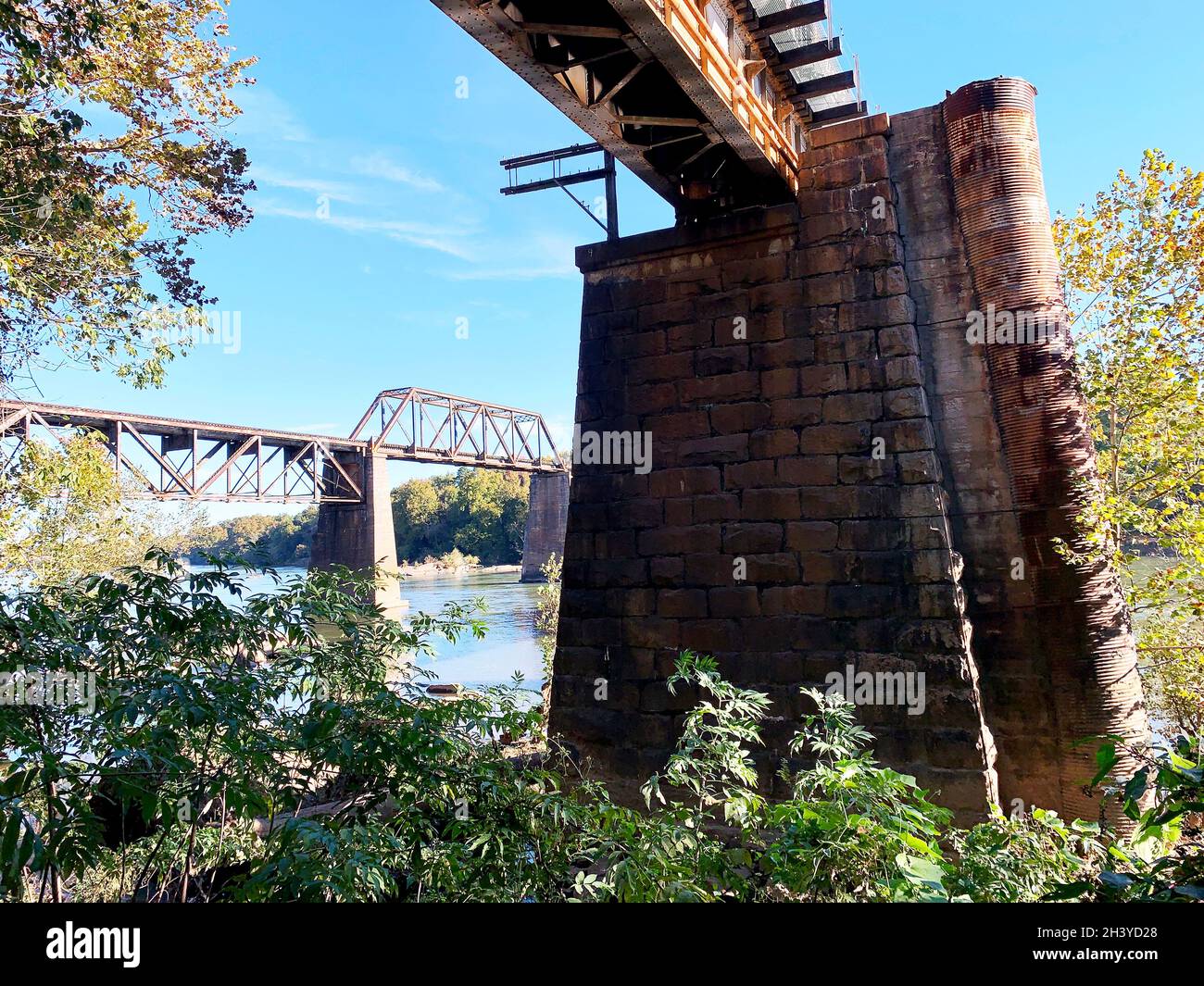 Eisenbahnkrümmer Brücken auf Stein- und Ziegelpiers über dem Fluss in der Sonne mit blauem Himmel Stockfoto