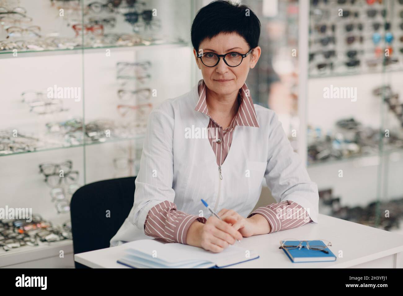 Schöner reifer Optiker, der im Augenoptiker-Salon ein Buch geschrieben hat Stockfoto