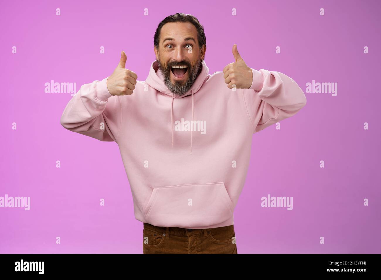 Aufgeregt energisch unterstützend charismatischen europäischen reifen bärtigen Mann in rosa Hoodie zeigen Daumen nach oben Geste lächelnd zustimmen approvi Stockfoto