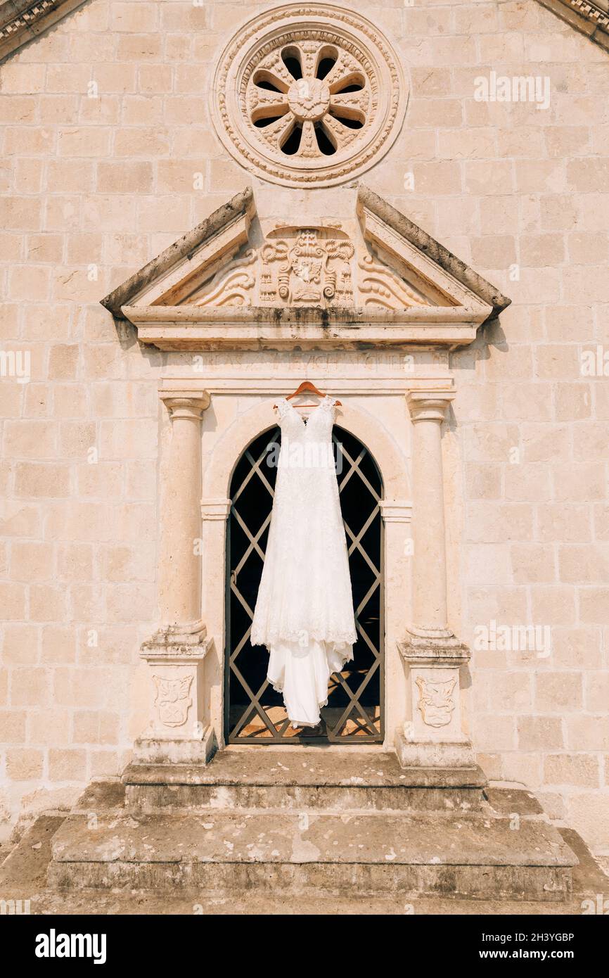 Das Hochzeitskleid hängt am Eingang der alten Kirche, zwischen den Säulen, unter der Rosette und den Flachreliefs. Stockfoto
