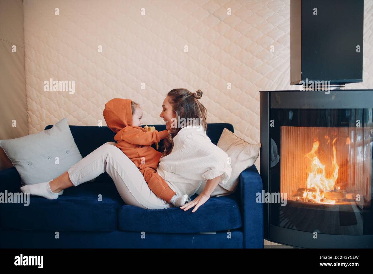 Mutter und Kind sitzen und spielen auf dem Sofa in der Nähe des Kamins. Mama und Baby. Eltern und kleine Kinder entspannen sich zu Hause. Familie hat Stockfoto