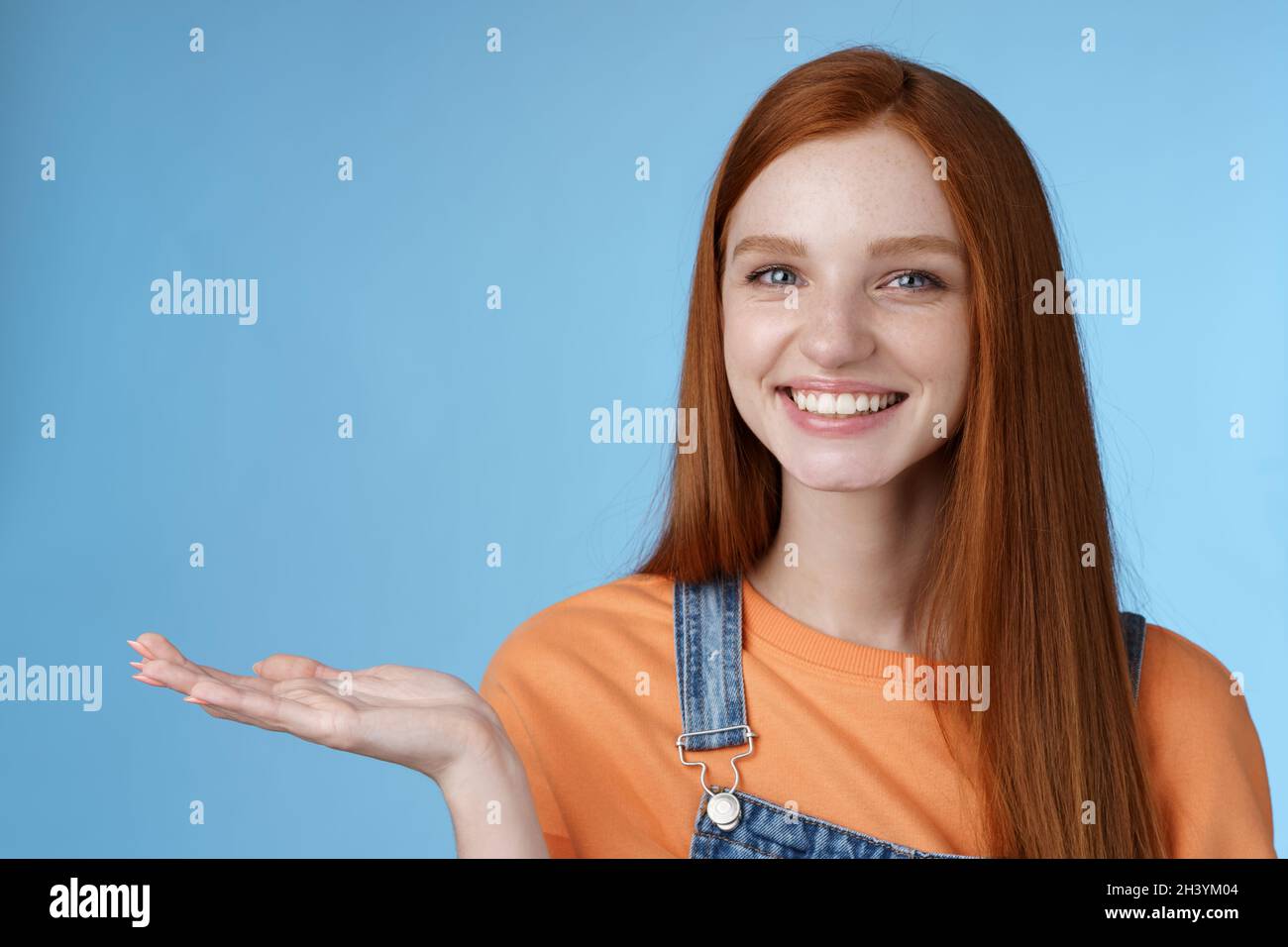 Stolz gut aussehende zuversichtlich Rotschopf Mädchen präsentieren genial Produkt halten Objekt Handfläche heben Hand leer blau kopieren Raum lächelnd Deli Stockfoto