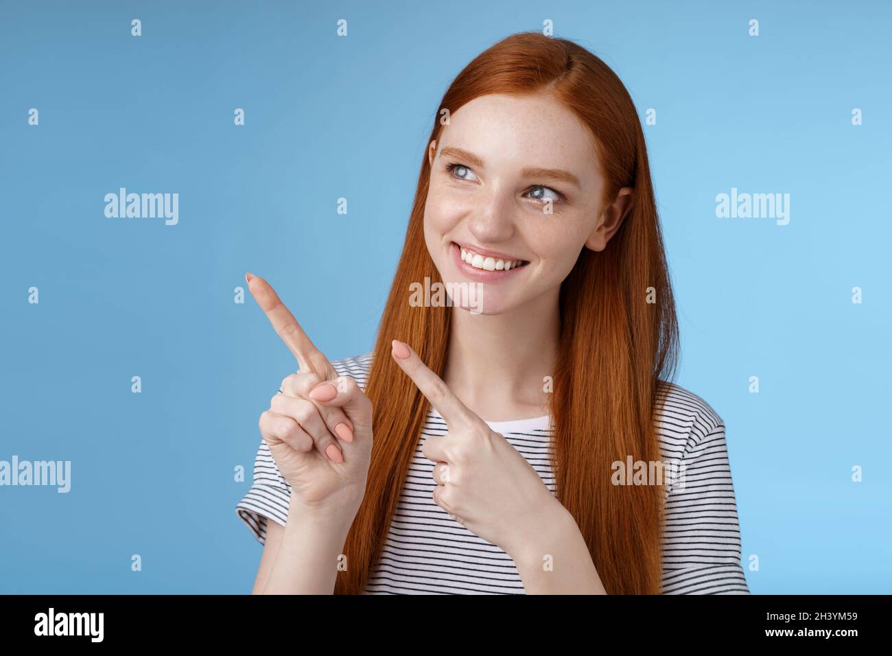 Attraktive rothaarige weibliche Modell reine saubere Haut Ingwer lange Haare zeigend suchen links fasziniert lächelnd zufrieden anzeigen in Stockfoto