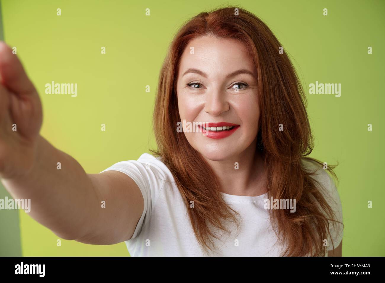 Nahaufnahme fröhlich enthusiastisch Rotschopf verführerische Frau mittleren Alters exandieren Arm zur Kamera nehmen Selfie-Smartphone lächelnd breit Stockfoto