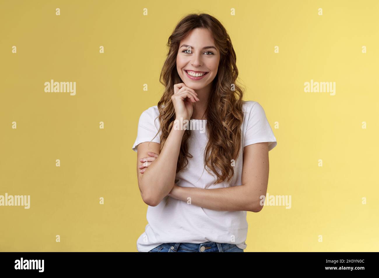 Zarte feminine enthusiastische charmante europäische Frau lockig lange Frisur lachend dummer Blick grinsend freudig berühren Kinn intri Stockfoto