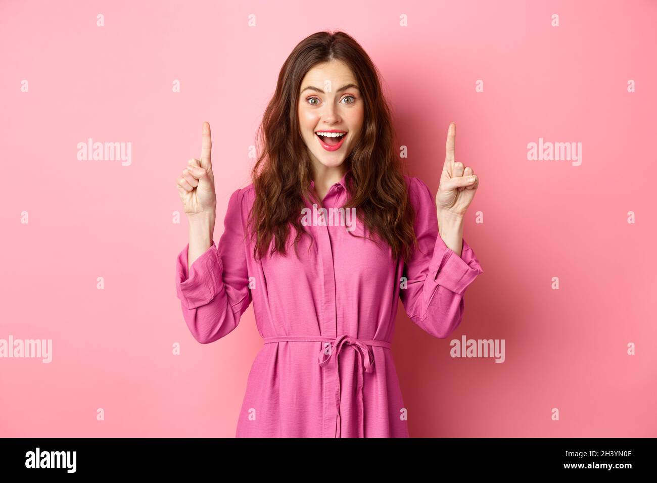 Attraktive glückliche Dame zeigt die Finger nach oben und lächelt fröhlich, zeigt ehrfürchtige Werbung, stehen über rosa Hintergrund Stockfoto