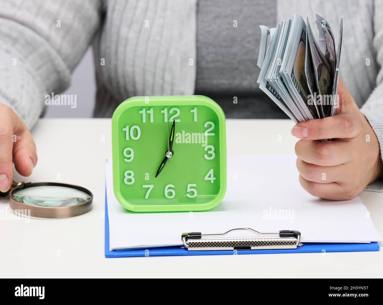 Stapel von hundert Dollar Scheinen in der Hand einer Frau und eine hölzerne Lupe auf einem weißen Tisch. Budgetanalyse, Einkommen und Stockfoto