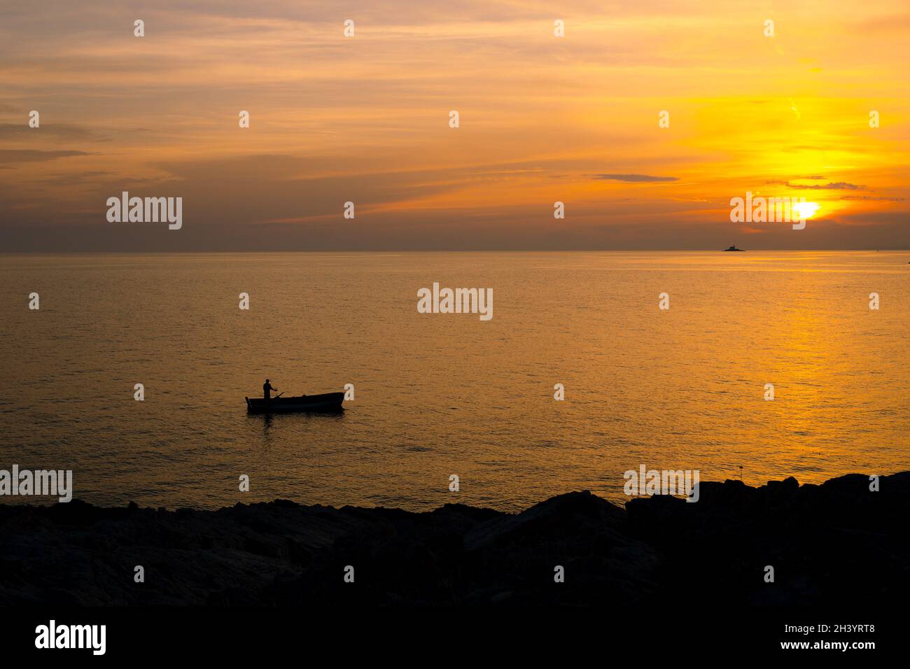 Ein Fischer auf einem Boot in der Nähe des Ufers vor dem Hintergrund eines goldenen Sonnenuntergangs. Stockfoto