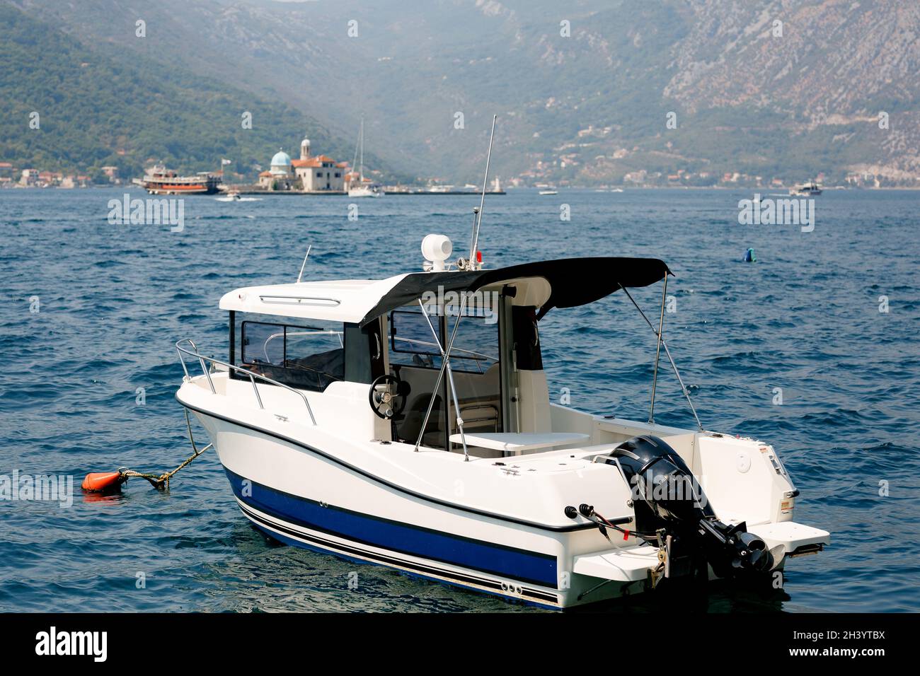 Motorboot, das in der Nähe der Stadt Perast vor der Kulisse der Berge und der Insel Gospa od Skrpella festgemacht ist. Stockfoto